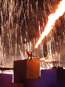 Cirque Bijou - A performer shoots a massive flame thrower into the air as pyro showers behind him