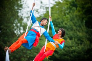 Cirque Bijou - Khoj - two circus performers swing from aerial silks hand in hand