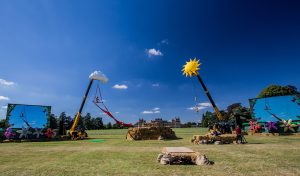 Cirque Bijou - Two Telehandlers raise a giant sun and cloud into the bright blue sky, two aerialists perform off them