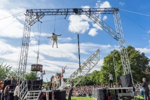 Cirque Bijou - Extraordinary Bodies perform their show Weighting in a green park in Bristol - a disabled perfromer flies above the set as the people below clap and cheer joyfully