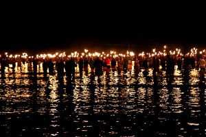 Cirque Bijou - As part of Battle for the Winds Olympic sailing event hundreds of people wade in to the sea carrying fire torches