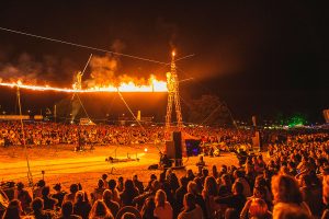 Cirque Bijou spectacle show for Wilderness Festival 2016 - A daring circus artist walks across a flaming high wire as crowds look up in amazement