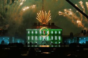 An aerialist in a flaming hoop, in front of video-mapped Dumfries house, lit all around with fireworks