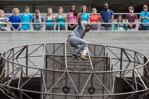 Extraordinary Bodies performer David Ellington swings from metal structure in What Am I Worth? National Theatre River Stage. Image Rob Harris.