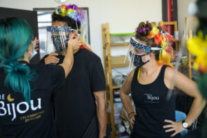 Two people are being dressed in very colourful masks and face visors