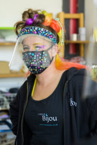 A woman with colourful hair wears a beautiful face mask and face visor