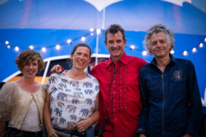 Four smiling people stand in front of a blue Big Top circus tent
