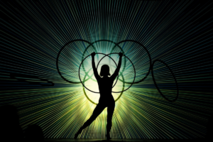 A woman stands silhouetted against a lit screen, holding a hula hoop above her head