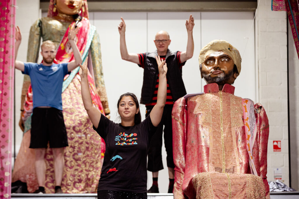 Rehearsals for Princess and the Chickpea at 101 Outdoor Arts. Artists perform with outreached arms in front of two large puppets