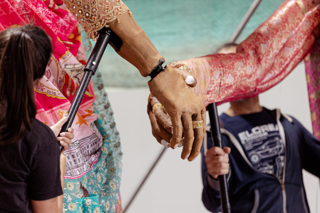 Rehearsals for Princess and the Chickpea at 101 Outdoor Arts. The hands of two giant puppets reach out to each other
