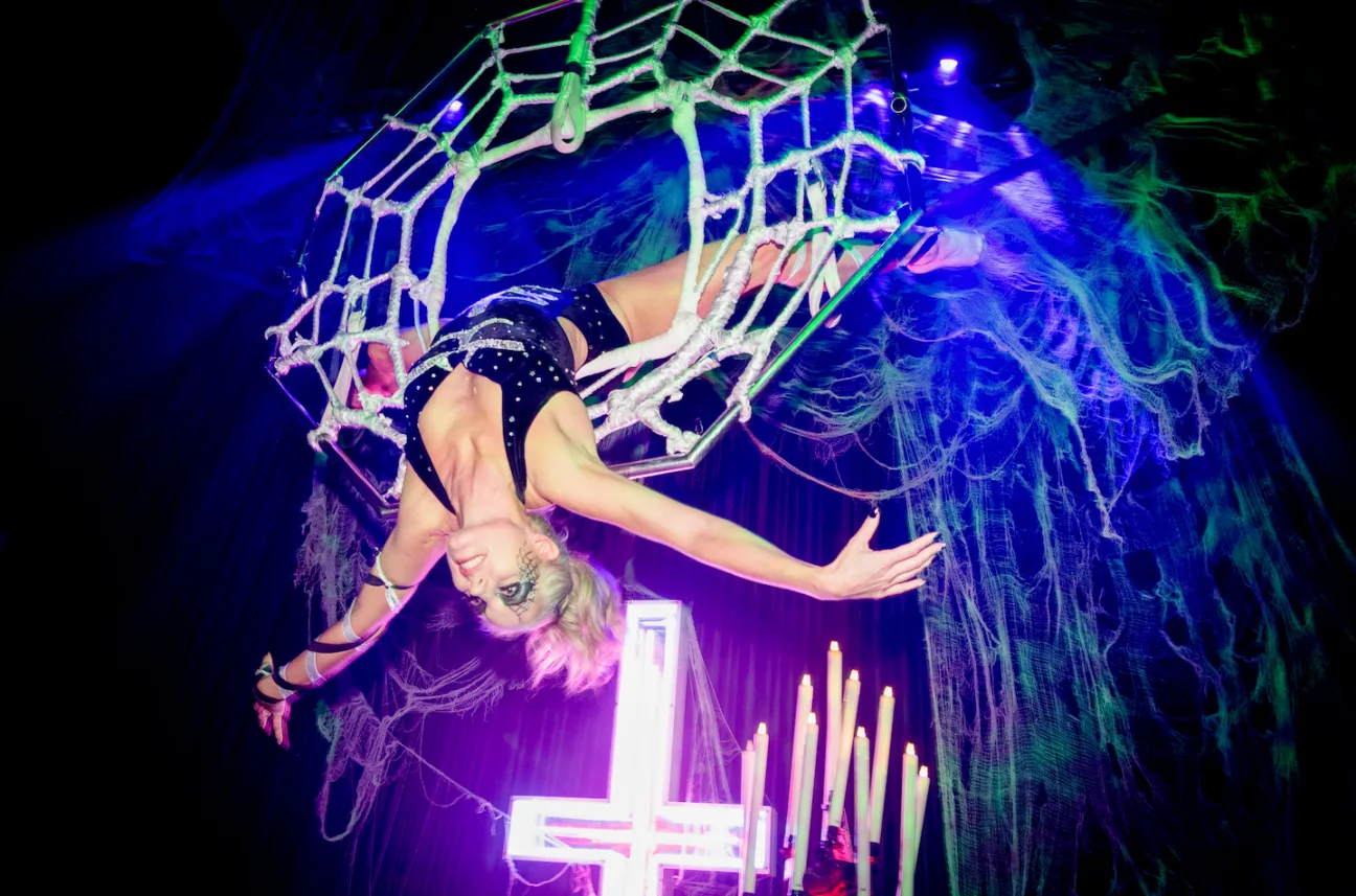 An aerialist hangs suspended from an aerial hoop decorated as a spiders web