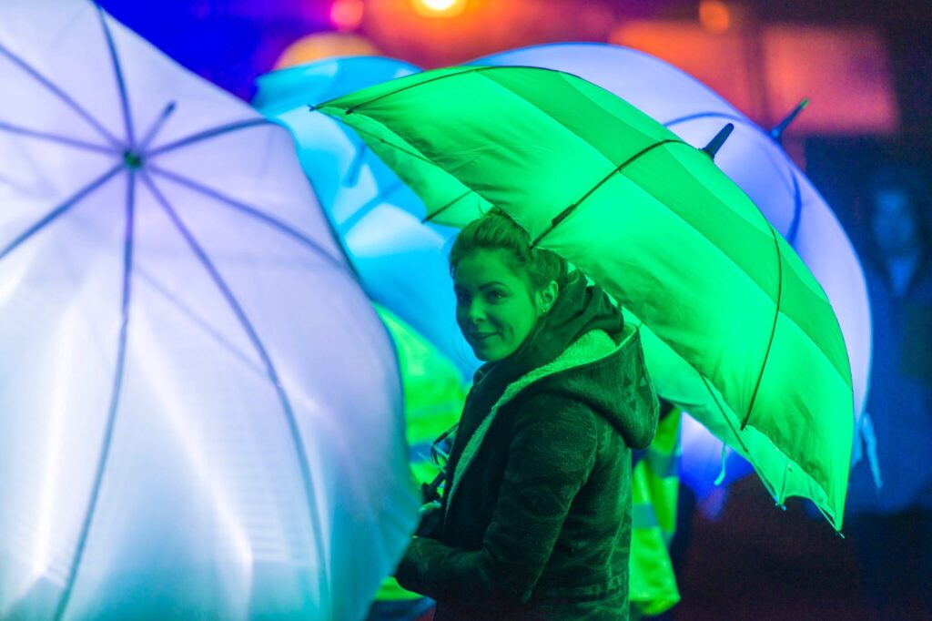 Celebrating 25 years of Cirque Bijou.  The picture is taken from their show launching Bristol Green Capital 2015.  A lady holds a green, LED umbrella. 