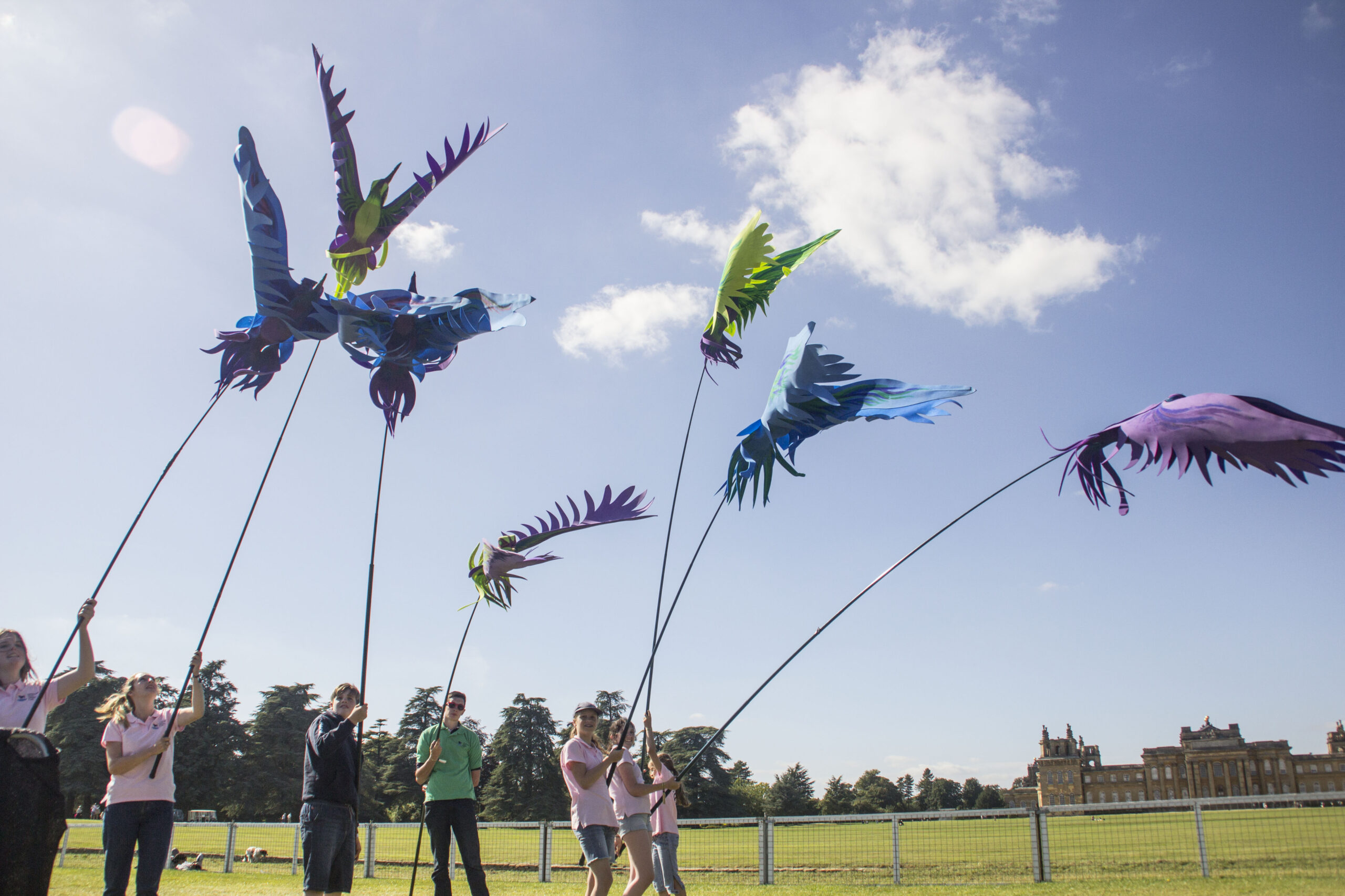 A flock of colourful bird puppets held up against a beautiful blue sky