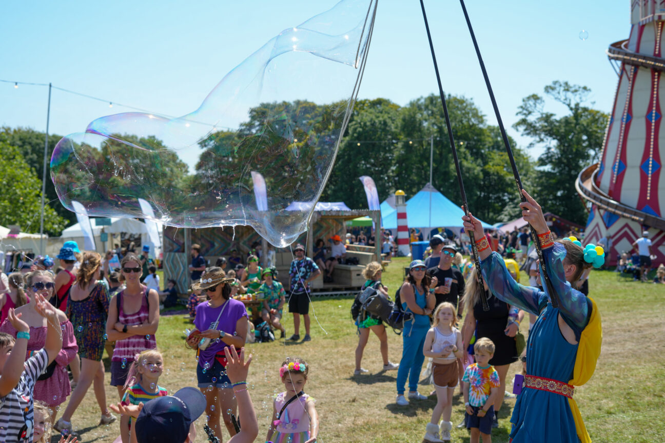 Camp Bestival bubble performer showing some children how to make a giant bubble