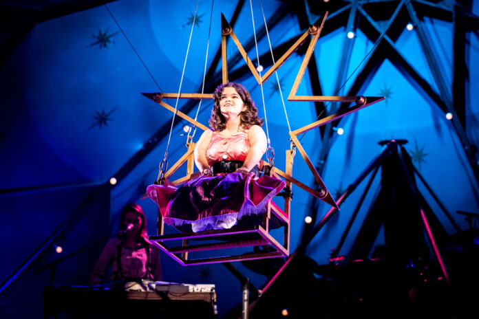 A woman sits atop an aerial circus prop with a star behind her