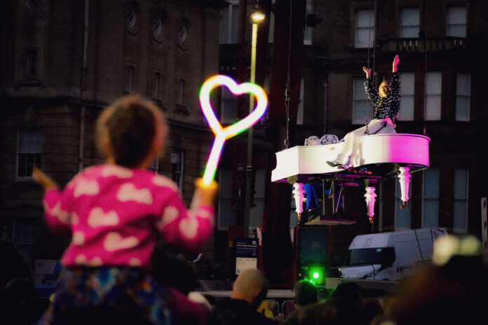 Child in the crowd looking up at Alba singing on a flying white piano