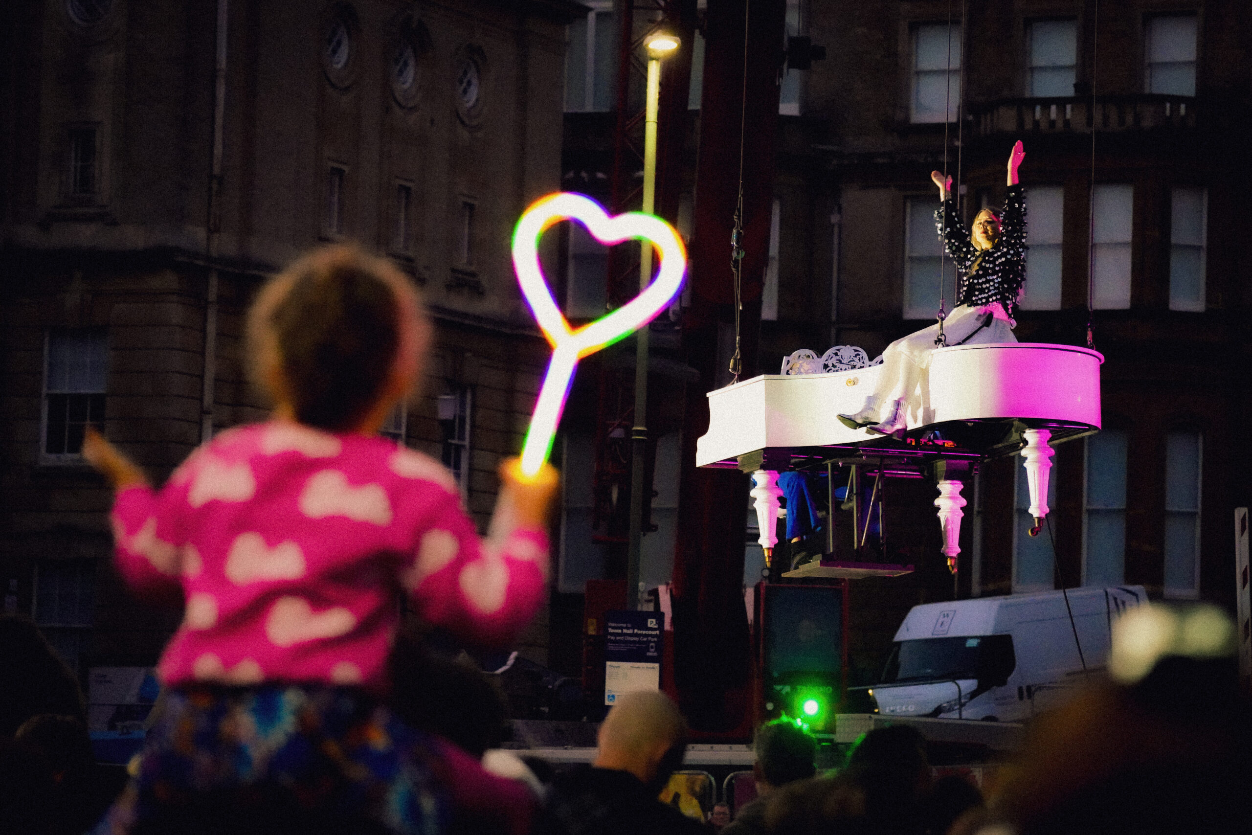 Child in the crowd looking up at Alba singing on a flying white piano
