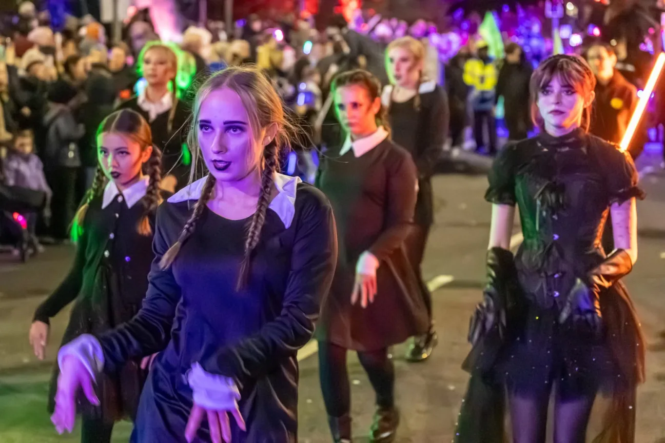 dance troupe all dressed as Wednesday Addams dancing in the parade