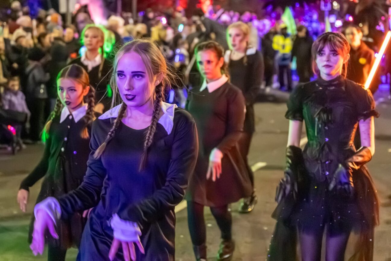 dance troupe all dressed as Wednesday Addams dancing in the parade