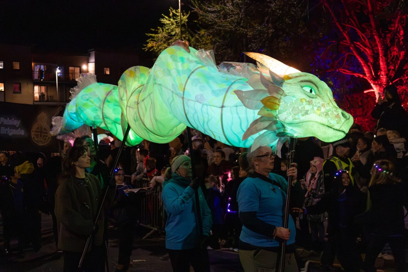 four people holding light up drag puppet in the parade