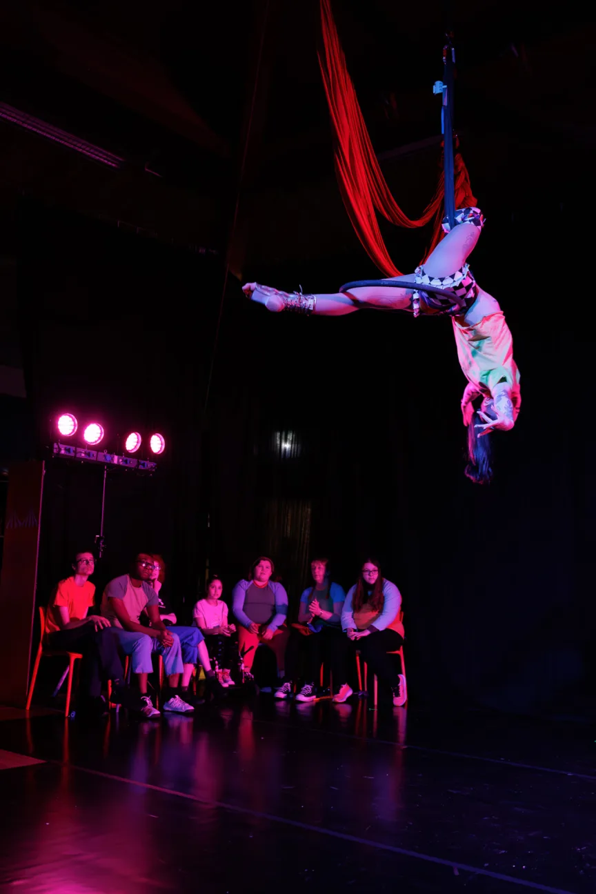 A group of young people on stage watching an aerial hoop performer