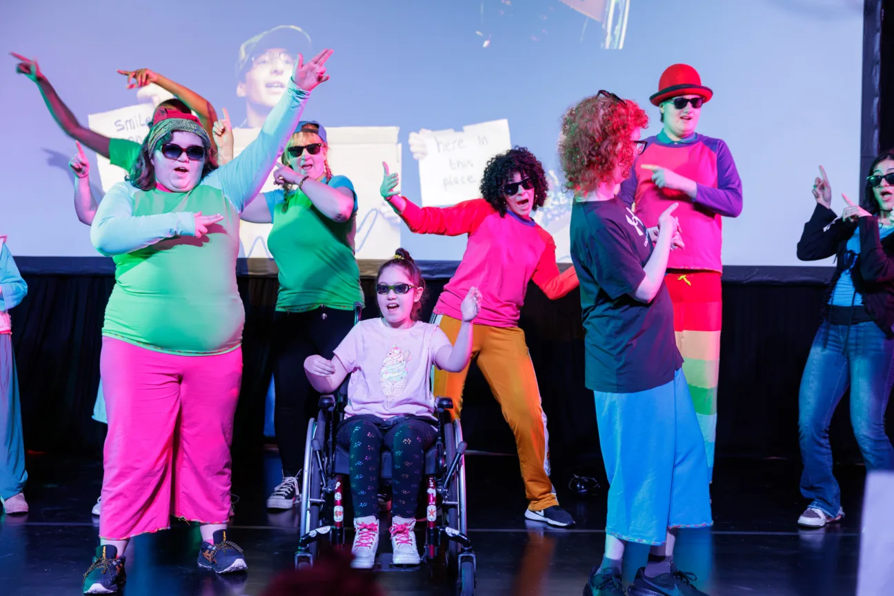 A wide shot of a group of young people dancing in brightly coloured clothes