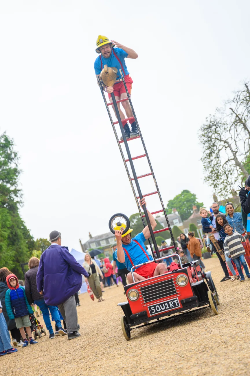 Two playful firemen on a small comedy fire truck car.