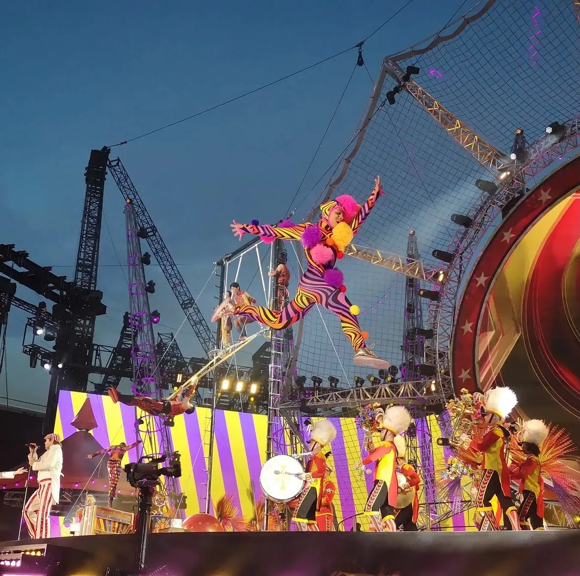 Photo of a trampoline performer covered in stripes and pom poms flying high on stage
