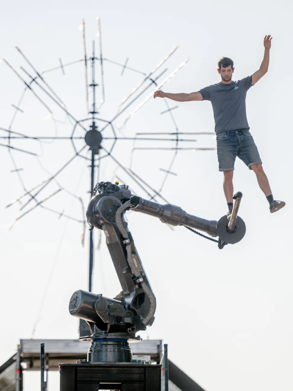 An acrobat balancing on a pole held by a robotic arm.