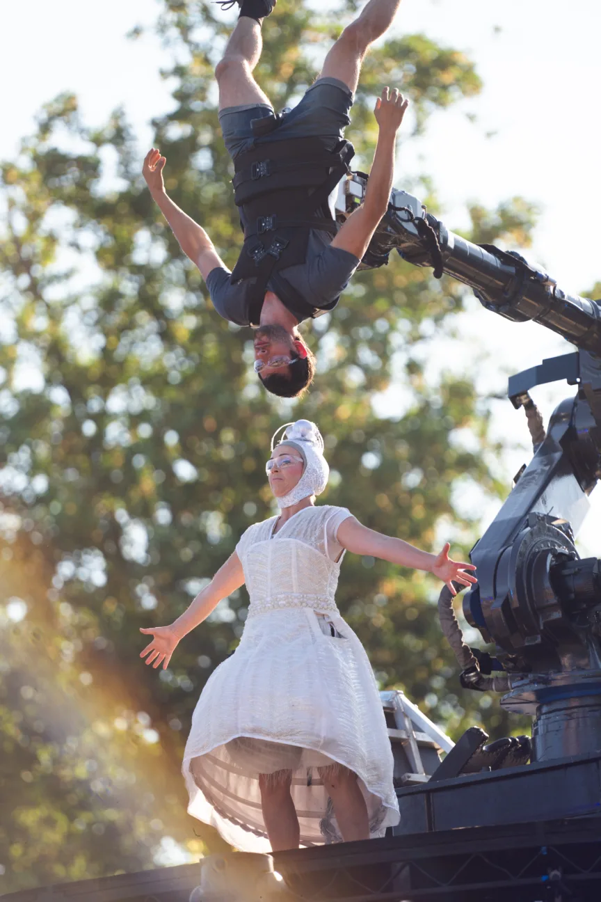 An acrobat held upside down on a robotic arm above a female performer wearing our LED dress.