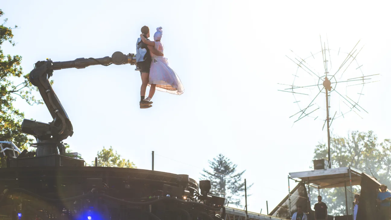 Large robotic arm holding two acrobats in a dancing embrace