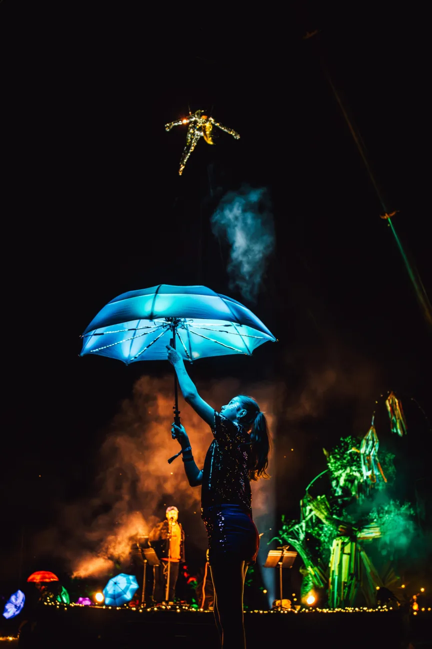 Girl with LED umbrella in foreground and an aerialist wearing our Mirrorball costume high above in the air