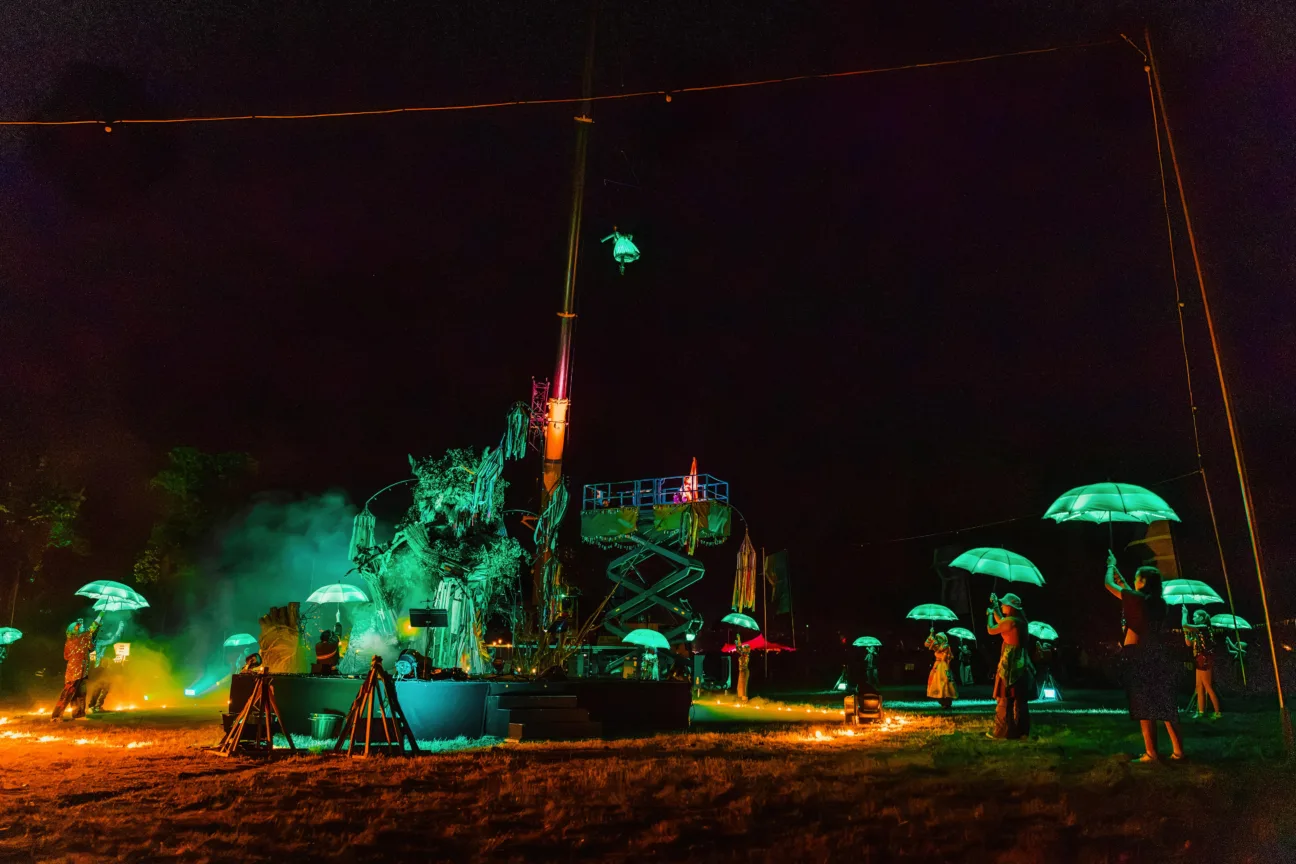 Wide shot of lots of performers with our LED Umbrellas all glowing green with an aerialist in our LED Dress flying high in the air also glowing green